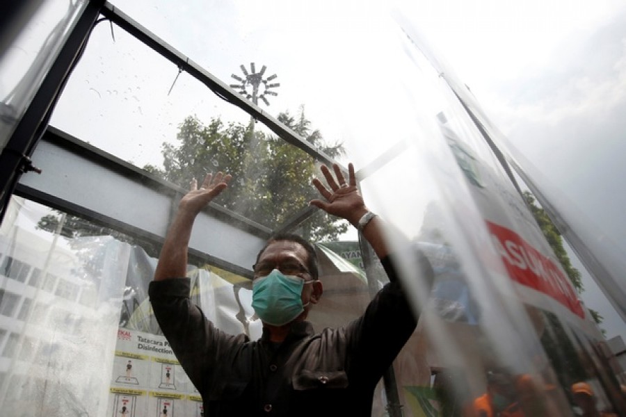 A man wearing face mask is sprayed inside a disinfection chamber, outside a shopping mall after Indonesia's capital begins a two-week emergency period to prevent the spread of coronavirus disease (COVID-19) in Jakarta, Indonesia, Mar 24, 2020. REUTERS