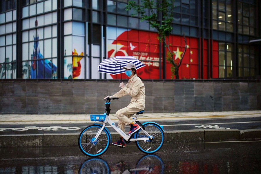A woman holding an umbrella rides a shared bicycle past an image of the Chinese flag after the lockdown was lifted in Wuhan, the capital of Hubei province and China's epicentre of the novel coronavirus disease (COVID-19) outbreak on April 10, 2020 — Reuters photo