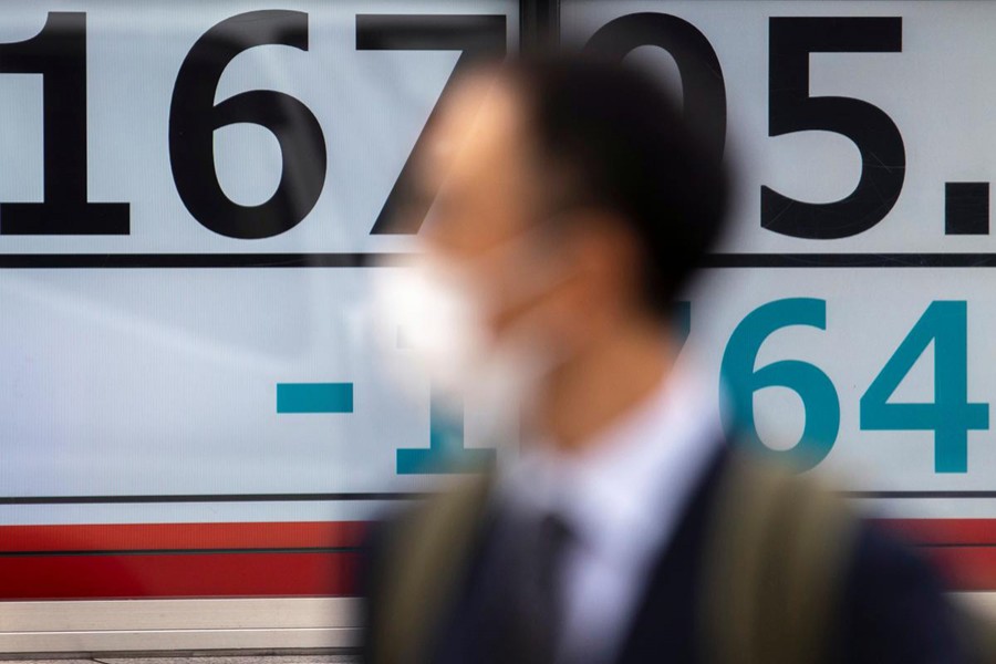 A man wearing a protective face mask, following an outbreak of coronavirus (COVID-19), walks past a screen showing the Nikkei index outside a brokerage in Tokyo, Japan on March 13, 2020 — Reuters/Files