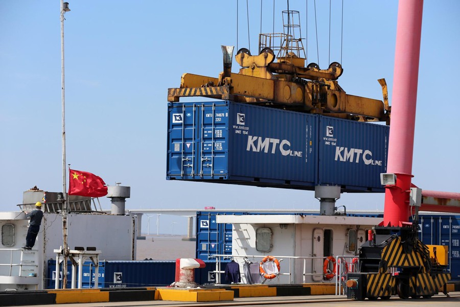 A crane lifts containers to be loaded onto a cargo vessel at a port in Qidong city of Nantong, Jiangsu province, China on March 16, 2020 — China Daily via REUTERS/Files