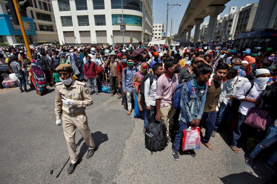 A policeman stands past migrant workers and their families waiting for transport to reach to a railway station to board trains to their home states, after a limited reopening of India's giant rail network following a nearly seven-week lockdown to slow the spreading of the coronavirus disease (COVID-19), in Ahmedabad, India, May 15, 2020. REUTERS/Amit Dave