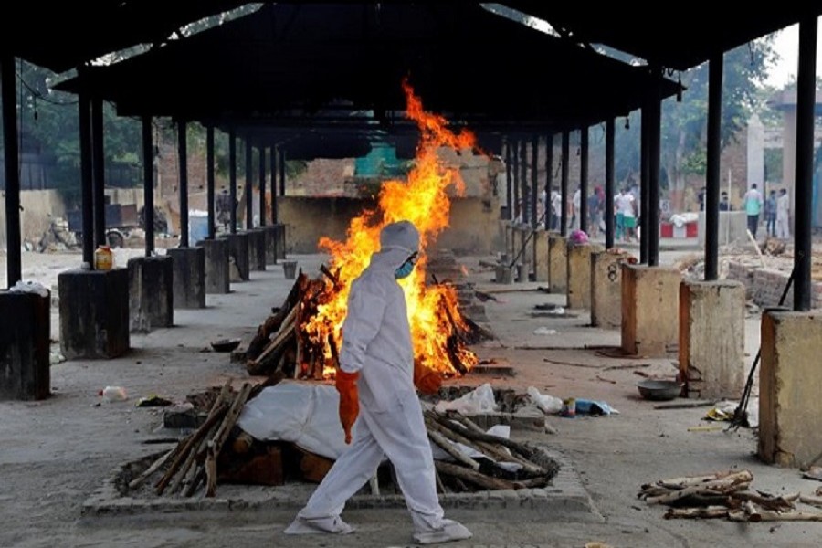 A priest wearing personal protective equipment (PPE) walks in front of the body of a person who died of the coronavirus disease (Covid-19), as he collects woods to make a funeral pyre at a crematorium in New Delhi, India, July 03, 2020 — Reuters