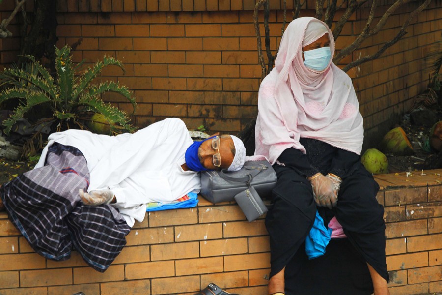 An elderly couple wearing protective masks and gloves rest outside Mugda General Hospital in the capital as they wait for Covid-19 test — File photo