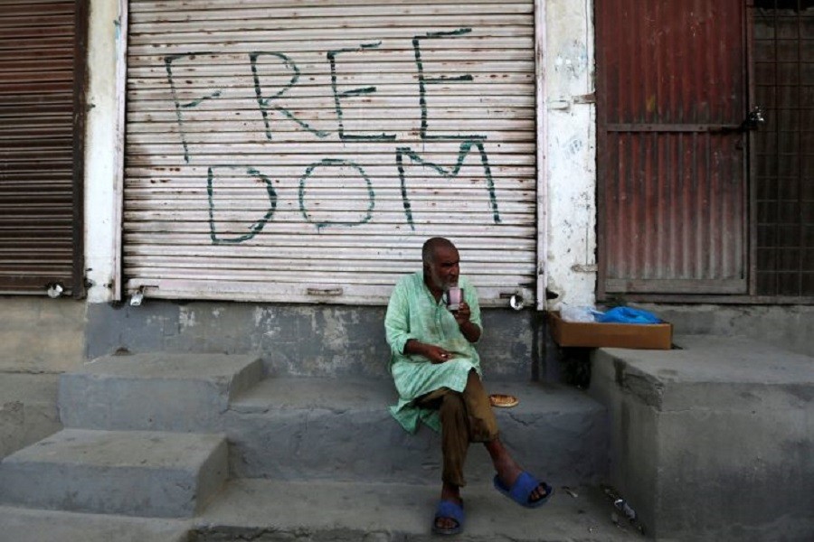 A Kashmiri man drinks tea in front of a closed shop painted with graffiti in Anchar neighbourhood in Srinagar July 28, 2020 — Reuters