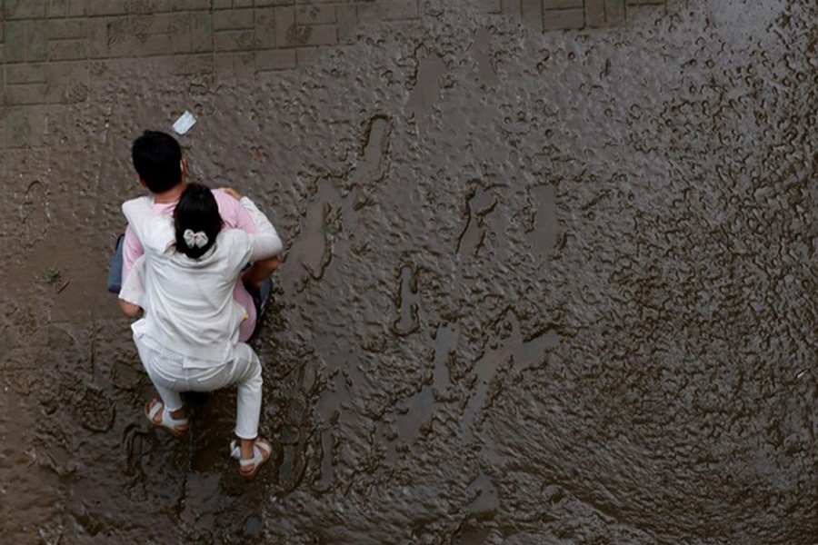 A man crosses a mud-covered trail carrying his wife on his back at a flooded Han River park in Seoul, South Korea, August 04, 2020. REUTERS   