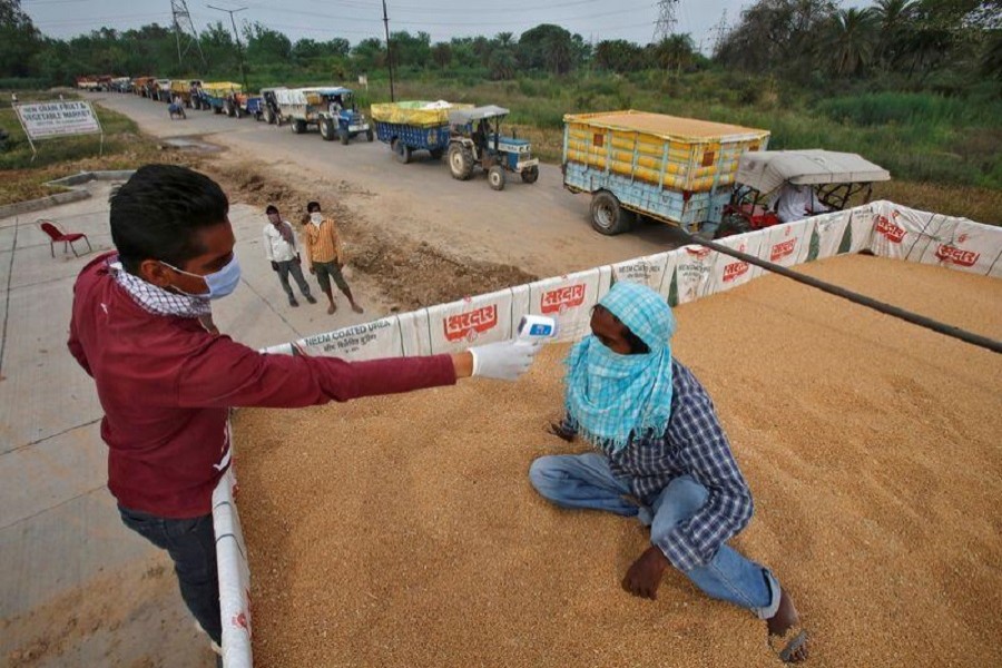 A health worker uses an infrared thermometer to check the temperature of a labourer sitting on wheat crop in a tractor trolley at an entry gate of a wholesale grain market, during a nationwide lockdown to slow the spreading of coronavirus disease (Covid-19) in Chandigarh, India, April 20, 2020 — Reuters/Files
