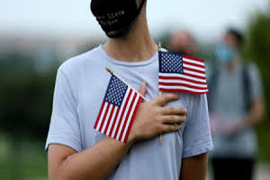 FILE PHOTO: An activist holds his hand over his heart in silence while holding American flags at sunrise to memorialize victims of the coronavirus disease (Covid-19) outbreak, near the Washington Monument in Washington, US, August 27, 2020. REUTERS/Tom Brenner