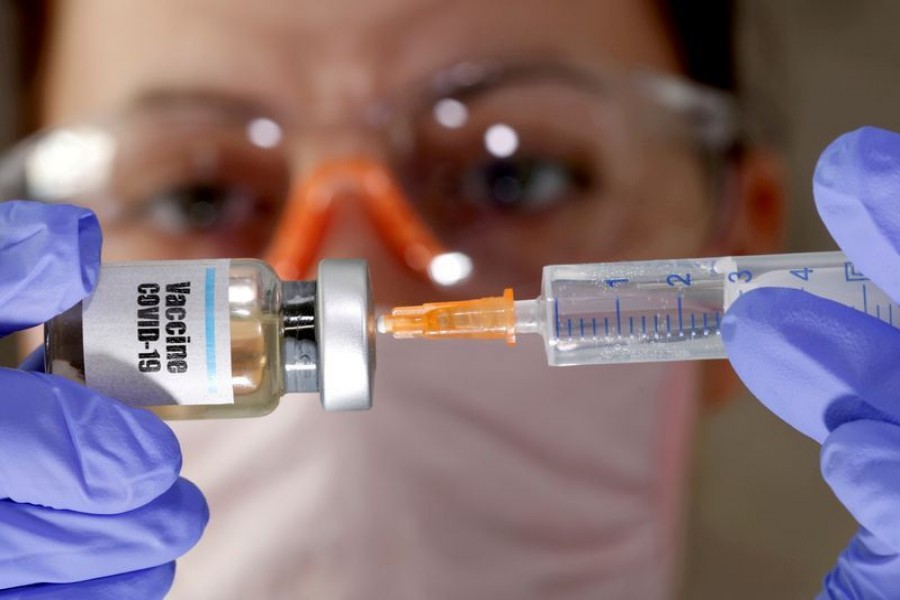 A woman holds a small bottle labeled with a "Vaccine COVID-19" sticker and a medical syringe in this illustration taken April 10, 2020. REUTERS/Dado Ruvic/File Photo