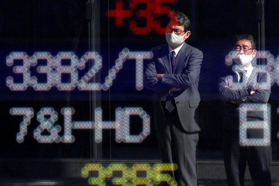 Passersby wearing protective face masks are reflected on a stock quotation board outside a brokerage, in Tokyo, Japan on November 10, 2020 — Reuters/Files