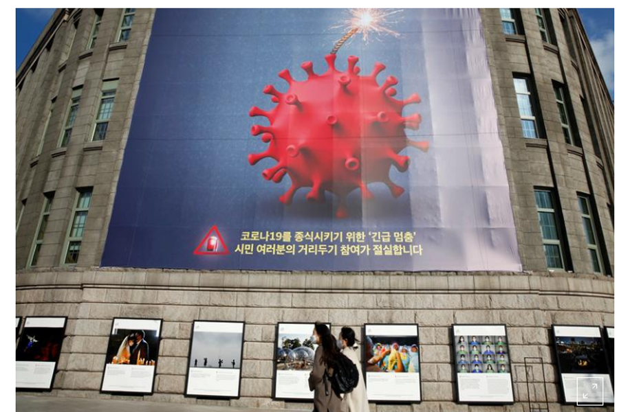 FILE PHOTO: Women wearing face masks walk past a banner promoting a social distancing campaign displayed on the wall of Seoul City Hall in Seoul, South Korea, November 27, 2020. REUTERS/Heo Ran