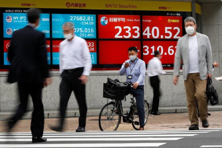 Passersby wearing protective face masks walk past a screen displaying Nikkei share average and world stock indexes outside a brokerage, amid the coronavirus disease (Covid-19) outbreak, in Tokyo, Japan October 5, 2020 — Reuters/Files