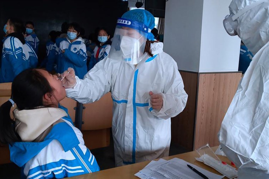 A medical worker in a protective suit collects a swab sample from a middle school student during a mass nucleic acid testing following a recent coronavirus disease (Covid-19) outbreak in Xingtai, Hebei province, China on January 6, 2021. China Daily via REUTERS/Files