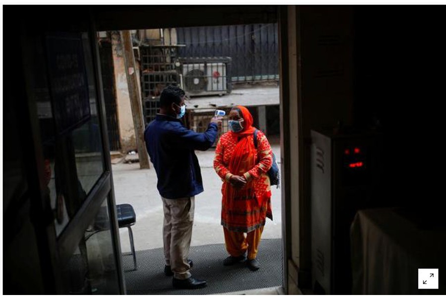 FILE PHOTO: A man checks the temperature of a woman, outside a vaccination centre, in New Delhi, India, February 13, 2021. REUTERS/Adnan Abidi