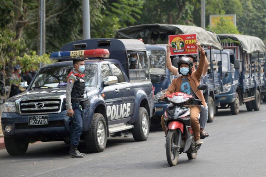 A demonstrator on a motorbike holds a placard while other demonstrator flashes the three-fingers salute as they ride past police officers during a protest against the military coup in Yangon, Myanmar on February 18, 2021 — Reuters