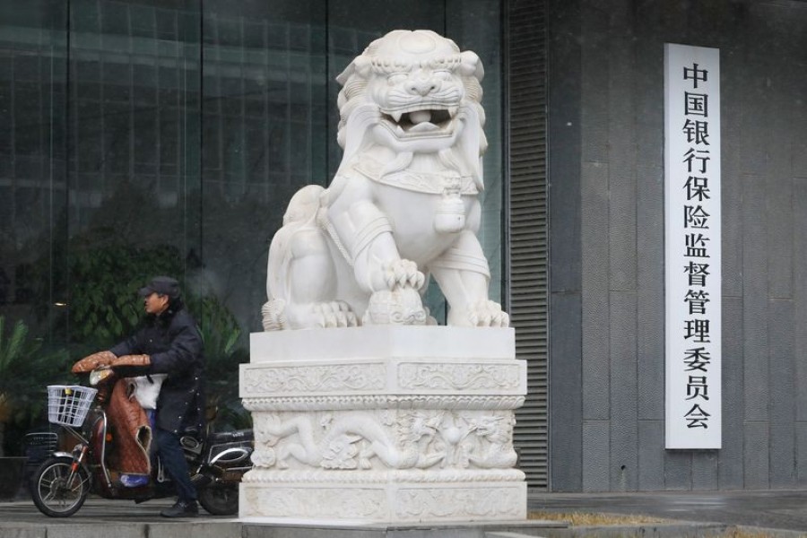 FILE PHOTO: A man rides an electric bike past the China Banking and Insurance Regulatory Commission (CBIRC) building in Beijing, China February 14, 2019. Picture taken February 14, 2019. REUTERS/Stringer