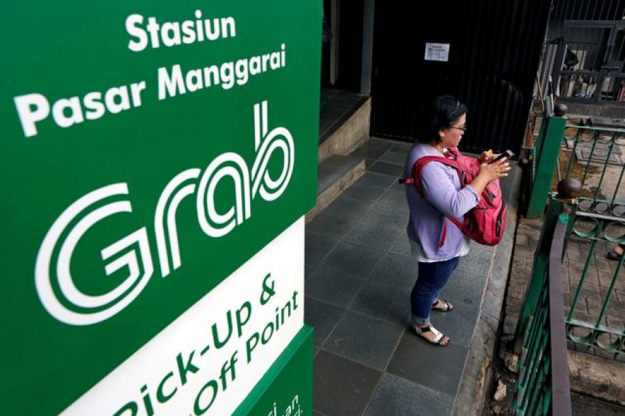 A woman uses her phone near a sign for the online ride-hailing service Grab at the Manggarai train station in Jakarta, Indonesia July 3, 2017. REUTERS/Agoes Rudianto/File Photo