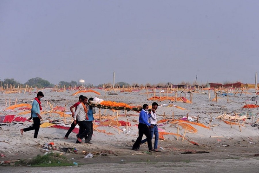 Relatives carry the body of a man for cremation after they, according to the relatives, were denied permission for his burial, past shallow sand graves of people, some of which are suspected to have died from the coronavirus disease (COVID-19), on the banks of the river Ganges in Shringaverpur on the outskirts of Prayagraj, India, May 21, 2021. Reuters