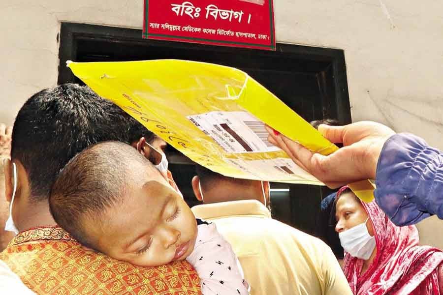 One-and-a-half-year-old Swadesh sleeps on his father's shoulder while his mother holds up a paper bag to shield the boy from the scorching sun, as they wait in a line to have his sample tested for coronavirus at Mitford Hospital in the city recently —FE file photo