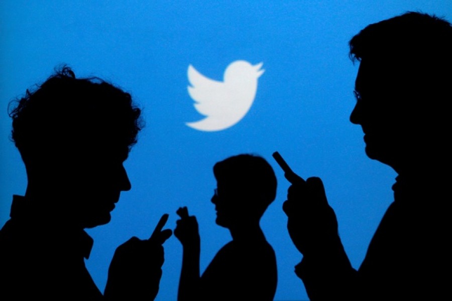 People holding mobile phones are silhouetted against a backdrop projected with the Twitter logo in this illustration picture taken September 27, 2013 — Reuters