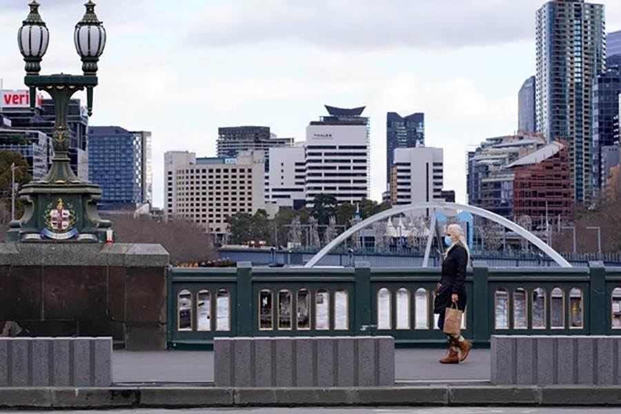 A lone woman, wearing a protective face mask, walks across an unusually quiet city centre bridge on the first day of a lockdown as the state of Victoria looks to curb the spread of a COVID-19 outbreak in Melbourne, Australia, July 16, 2021. REUTERS