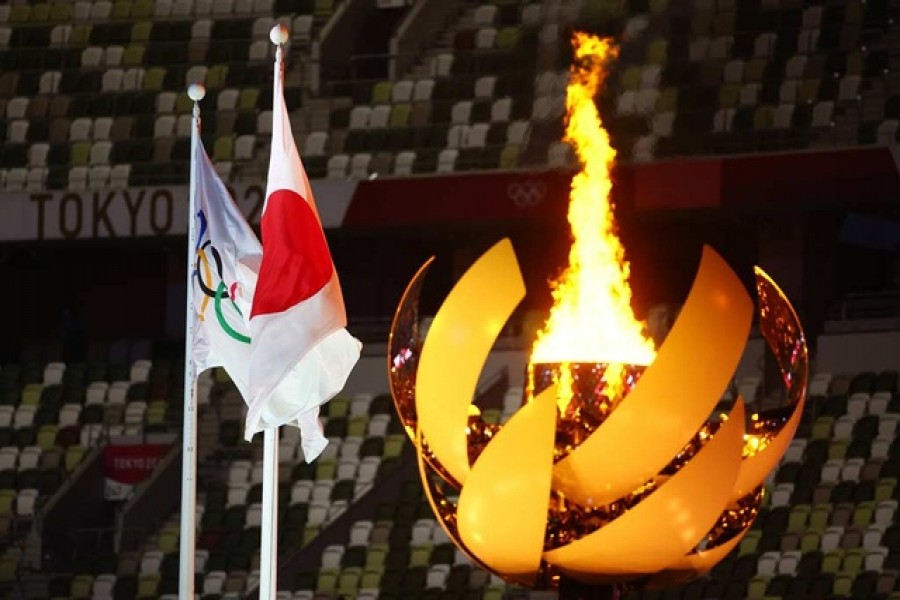 The Olympic flame is seen lit in the cauldron at the opening ceremony alongside a flag of Japan and the Olympic flag. Olympic Stadium, Tokyo, Japan - July 23, 2021 — Reuters