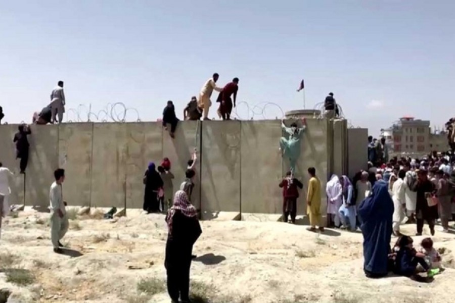 People climb a barbed wire wall to enter the airport in Kabul, Afghanistan August 16, 2021, in this still image taken from a video. REUTERS TV/via REUTERS