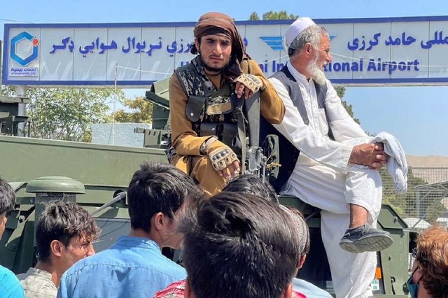 A member of Taliban forces (L) sits on an armoured vehicle outside Hamid Karzai International Airport in Kabul, Afghanistan August 16, 2021. REUTERS