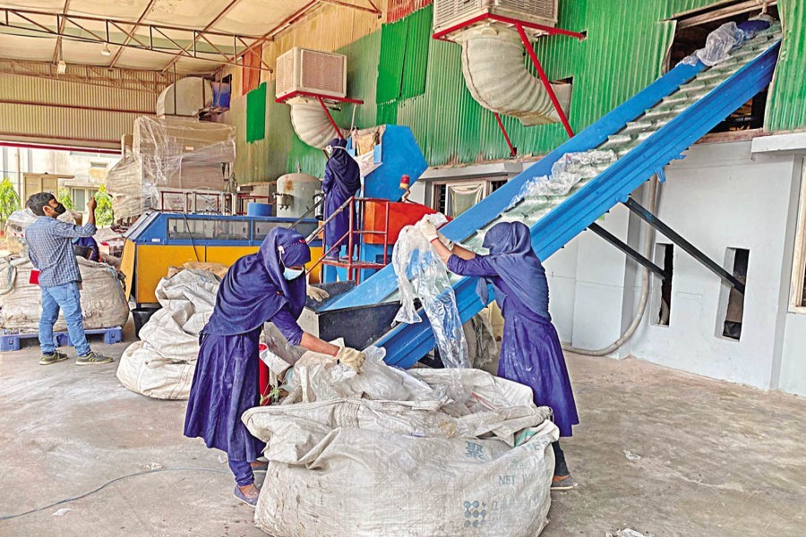 Workers putting used plastics on a conveyor belt for crushing at the recycling plant of Pran-RFL Group in Habiganj — FE Photo