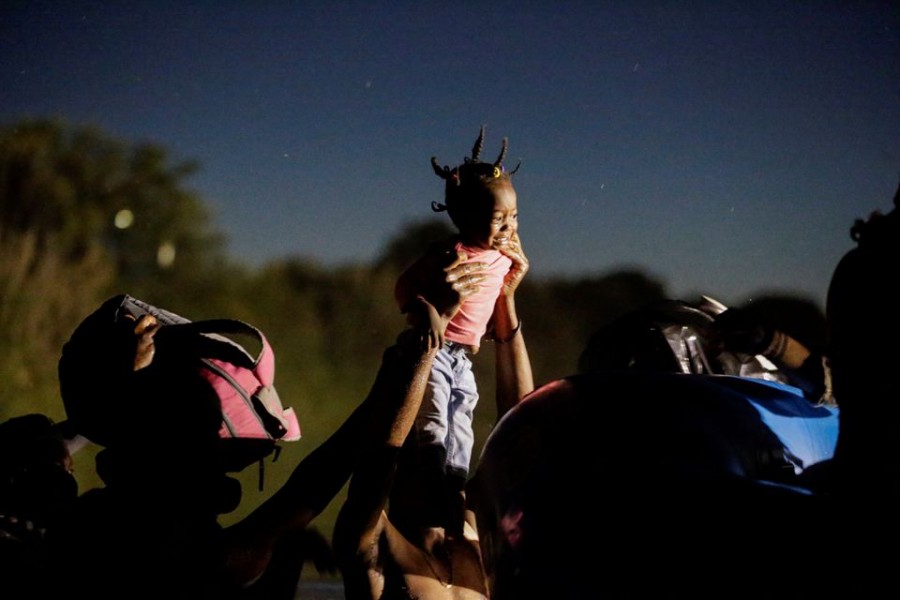 Migrants seeking refuge in the US and crossing the Rio Grande river towards Del Rio, Texas, US, hold up a girl to be helped by Border Patrol Agents on an inflatable boat, as seen from Ciudad Acuna, Mexico, September 23, 2021. REUTERS/Daniel Becerril