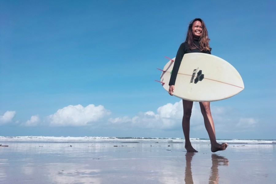 A surfing business owner, 38-year-old, Halfia Lando poses holding a surfboard at a Kuta beach as Indonesia opens up the tourist island of Bali to some countries including China, New Zealand, and Japan from Oct 14, visitors are still required to quarantine for eight days at their own expense, in Denpasar, Bali, Indonesia, Oct 12, 2021. REUTERS/Sultan Anshori