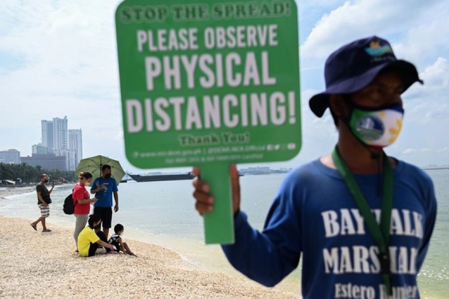 A person holds a placard reminding people to observe physical distancing as they visit the newly reopened portion of Manila Bay filled with artificial white sand, as the country's capital region loosens coronavirus disease (COVID-19) restrictions, in Manila, Philippines, October 16, 2021. REUTERS/Lisa Marie David