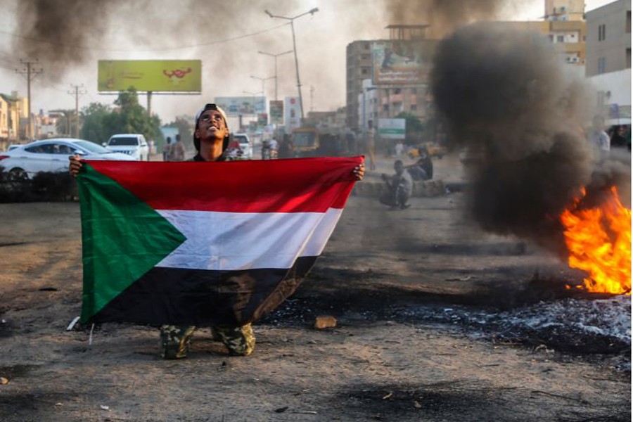 -- A Sudanese protester holds the national flag next to burning tyres during a demonstration in the capital, Khartoum, Sudan, on October 26, 2021 [Mohammed Abu Obaid/EPA]