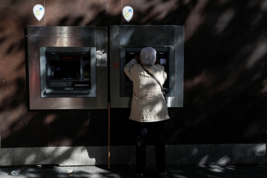 A woman uses a Caixabank branch ATM machine displaying logos of both Caixabank and Bankia banks in Madrid, Spain, November 10, 2021 – Reuters/Files