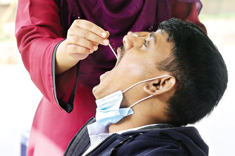 A health official collects a mouth swab sample from a man at a coronavirus testing centre of the Mugda Medical College and Hospital in Dhaka on Monday. With the Covid cases increasing these days, more people are turning to the health facility to have their samples tested for the virus — FE photo by KAZ Sumon