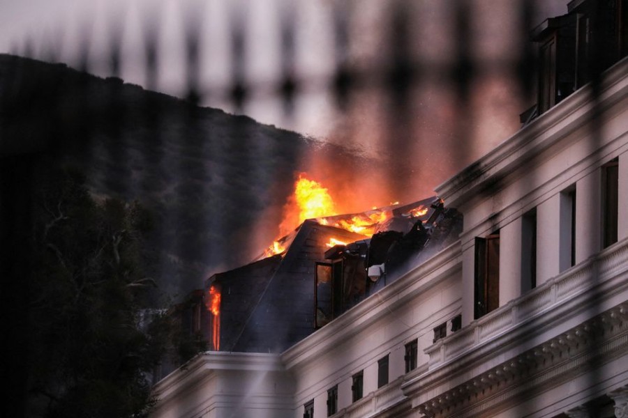 Flames and smoke rise over the roof of the National Assembly building as the fire at the parliament flared up again, in Cape Town, South Africa, January 3, 2022. Picture taken through a fence. REUTERS/Sumaya Hisham