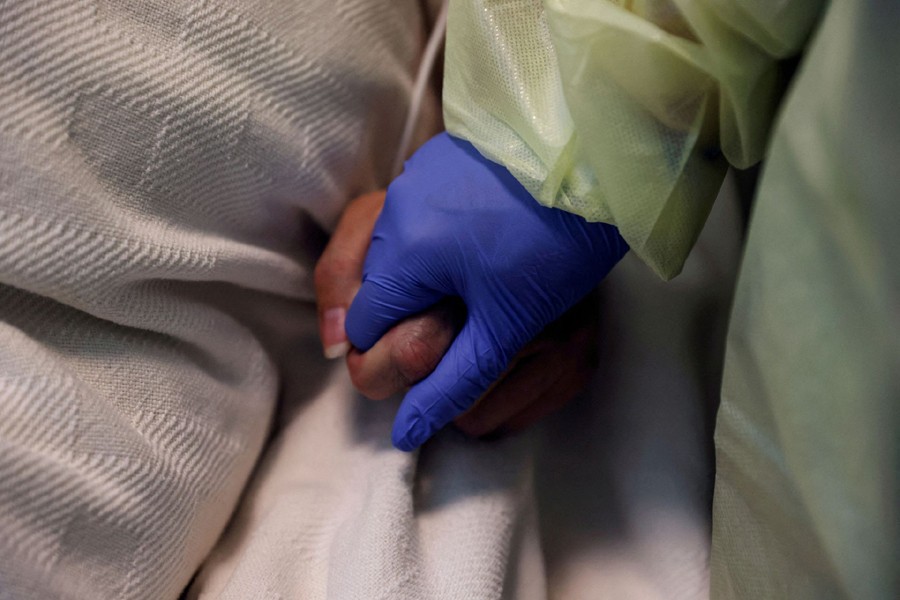 A woman in her personal protective equipment (PPE) gear holds the hand of a coronavirus disease (Covid-19) positive patient, in her isolation room at Madison Memorial Hospital in Rexburg, Idaho, US on October 28, 2021 — Reuters/Files
