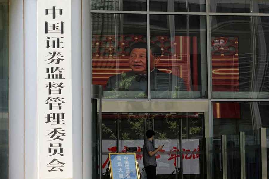 A man stands near a screen showing news footage of Chinese President Xi Jinping at the China Securities Regulatory Commission (CSRC) building on the Financial Street in Beijing, China July 9, 2021 — Reuters/Tingshu Wang