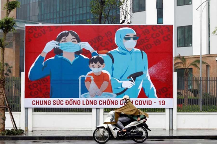 A man wears a protective mask as he rides past a propaganda banner promoting prevention against COVID-19 in Hanoi, Vietnam Apr 3, 2020. Reuters