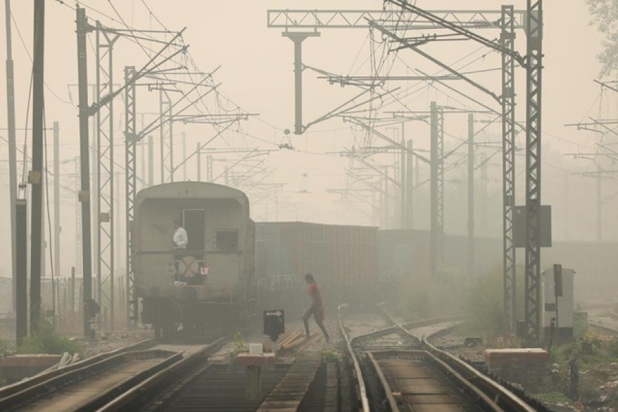 A woman crosses railway tracks as a goods train passes by, on a smoggy day in New Delhi, India, Nov 12, 2021. REUTERS/Anushree Fadnavis