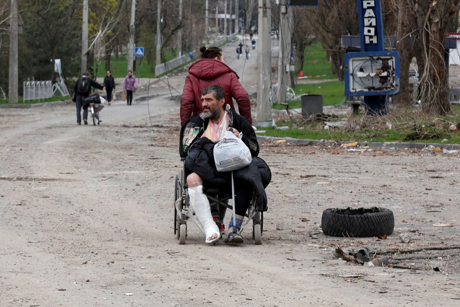 A woman pulls a wheel chair while transporting an injured man in a street in the course of Ukraine-Russia conflict in the southern port city of Mariupol, Ukraine on April 18, 2022 — Reuters photo