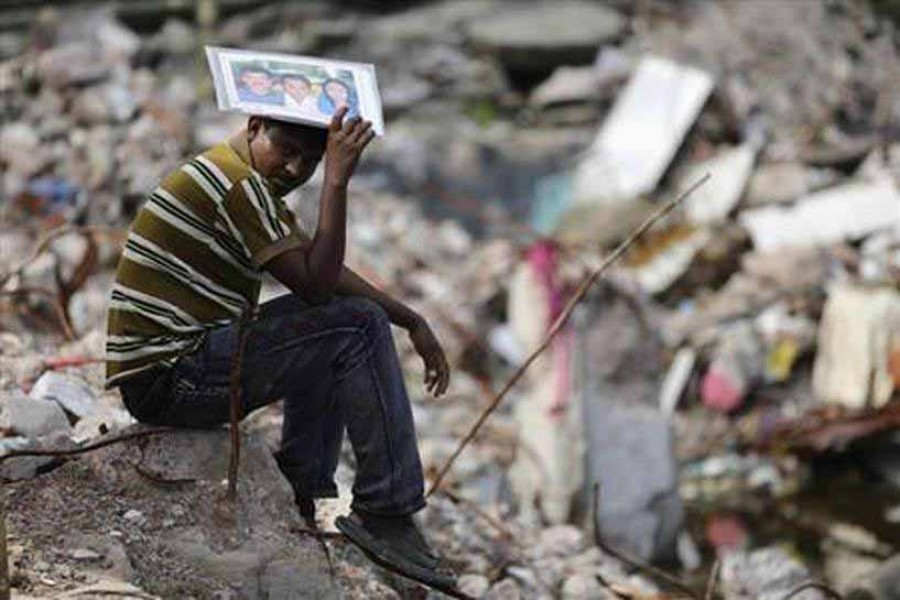 Abdur Rahman holds a picture of his wife Cahyna Akhter, a garment worker who died in the Rana Plaza building collapse incident, as he sits in front of the site in Savar August 2, 2013 – Reuters/Andrew Biraj