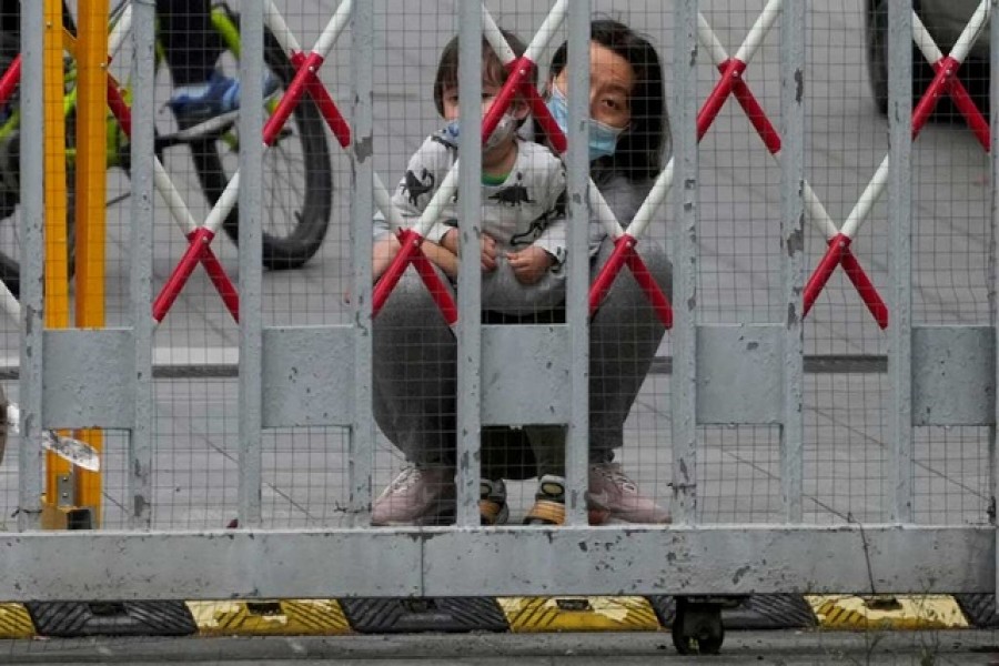 A resident and a child look out through gaps in the barriers at a closed residential area during lockdown, amid the coronavirus disease (COVID-19) pandemic, in Shanghai, China, May 10, 2022. Reuters