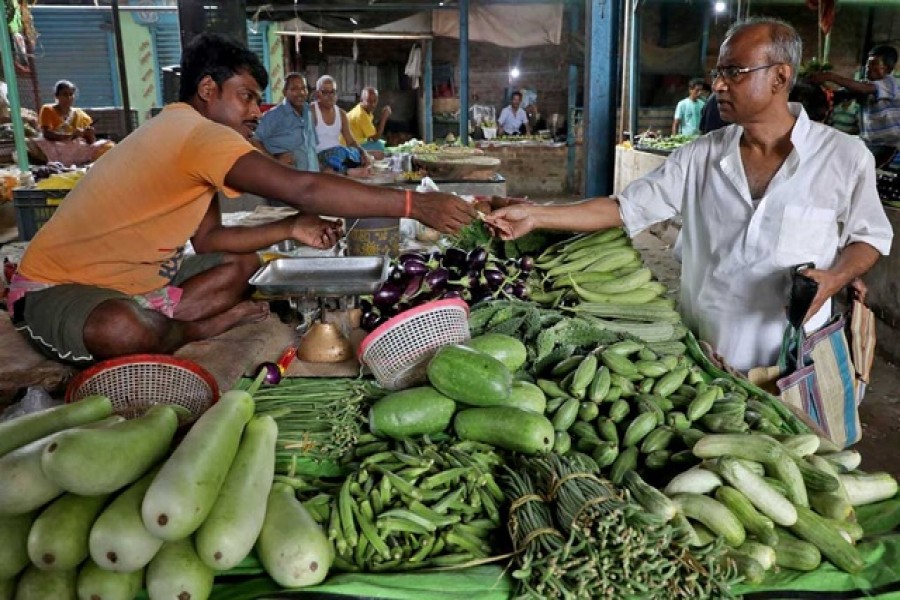 Nikhil Kumar Mondal, 65, a retired school headmaster, buys vegetables from a vendor at a market on the outskirts of Kolkata, India, May 20, 2022. REUTERS