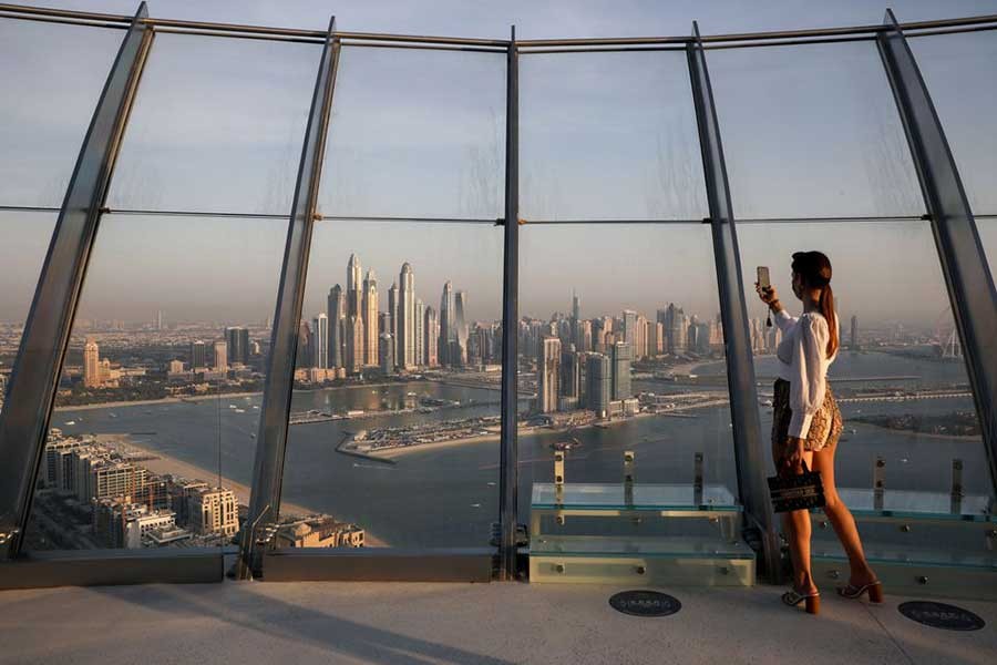A woman takes a picture with a smartphone of the upscale Marina district from the Palm Tower in Dubai of United Arab Emirates (UAE]) last year. The UAE is expected to attract the largest net inflows of millionaires globally in 2022. –Reuters file photo