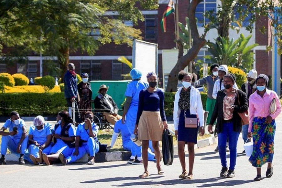 People walk past Zimbabwean medical workers as they sit outside Sally Mugabe Hospital during a strike by state doctors and nurses to press for higher pay, in Harare, Zimbabwe, June 20, 2022. REUTERS/Philimon Bulawayo
