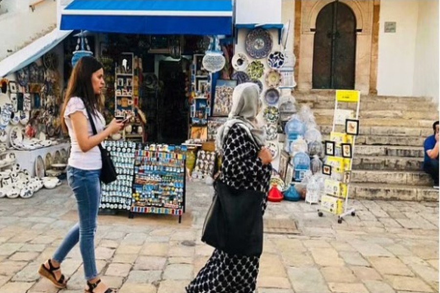 Two Tunisian women walk past a souvenir shop in Sidi Bou Said north of Tunis on June 17, 2019. Menna A Farouk