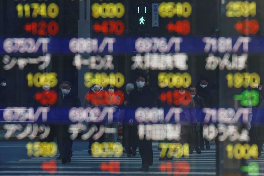 Pedestrians wearing protective masks, amid the coronavirus disease (COVID-19) outbreak, are reflected on an electronic board displaying various company’s stock prices outside a brokerage in Tokyo, Japan, February 25, 2022. REUTERS/Kim Kyung-Hoon