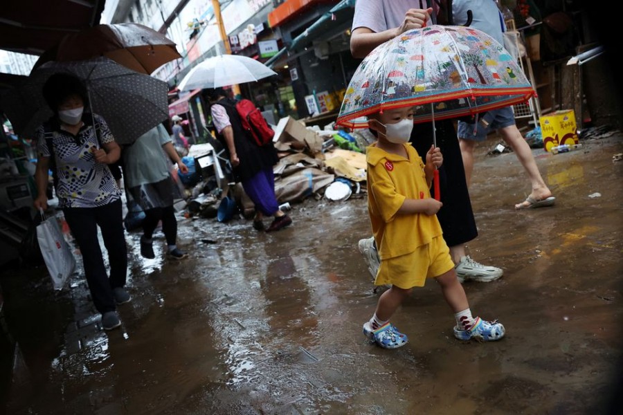 A boy using an umbrella makes his way through a road that was flooded after torrential rain at a traditional market in Seoul, South Korea, August 9, 2022. REUTERS/Kim Hong-Ji