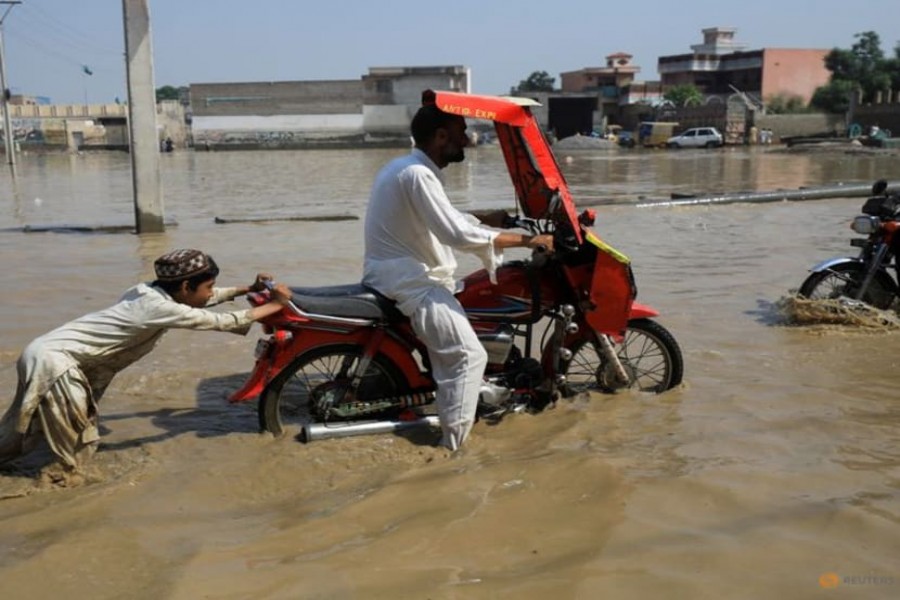 A boy pushes a motorbike after it stopped amid flood water, following rains and floods during the monsoon season in Nowshera, Pakistan August 30, 2022. REUTERS/Fayaz Aziz