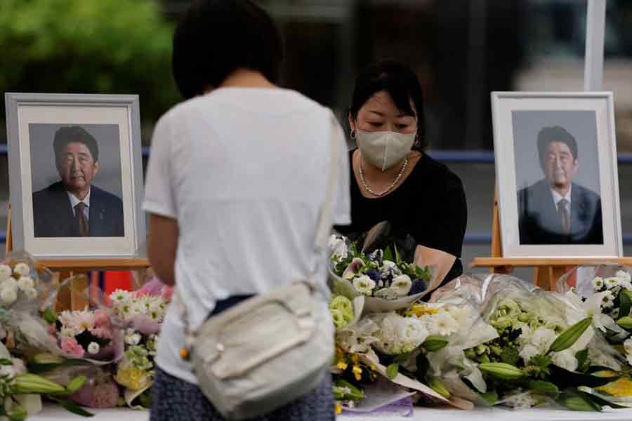 A mourner offering flowers next to pictures of late former Japanese Prime Minister Shinzo Abe, who was shot while campaigning for a parliamentary election, on the day to mark a week after his assassination at the Liberal Democratic Party headquarters in Tokyo on July 15 this year –Reuters file photo